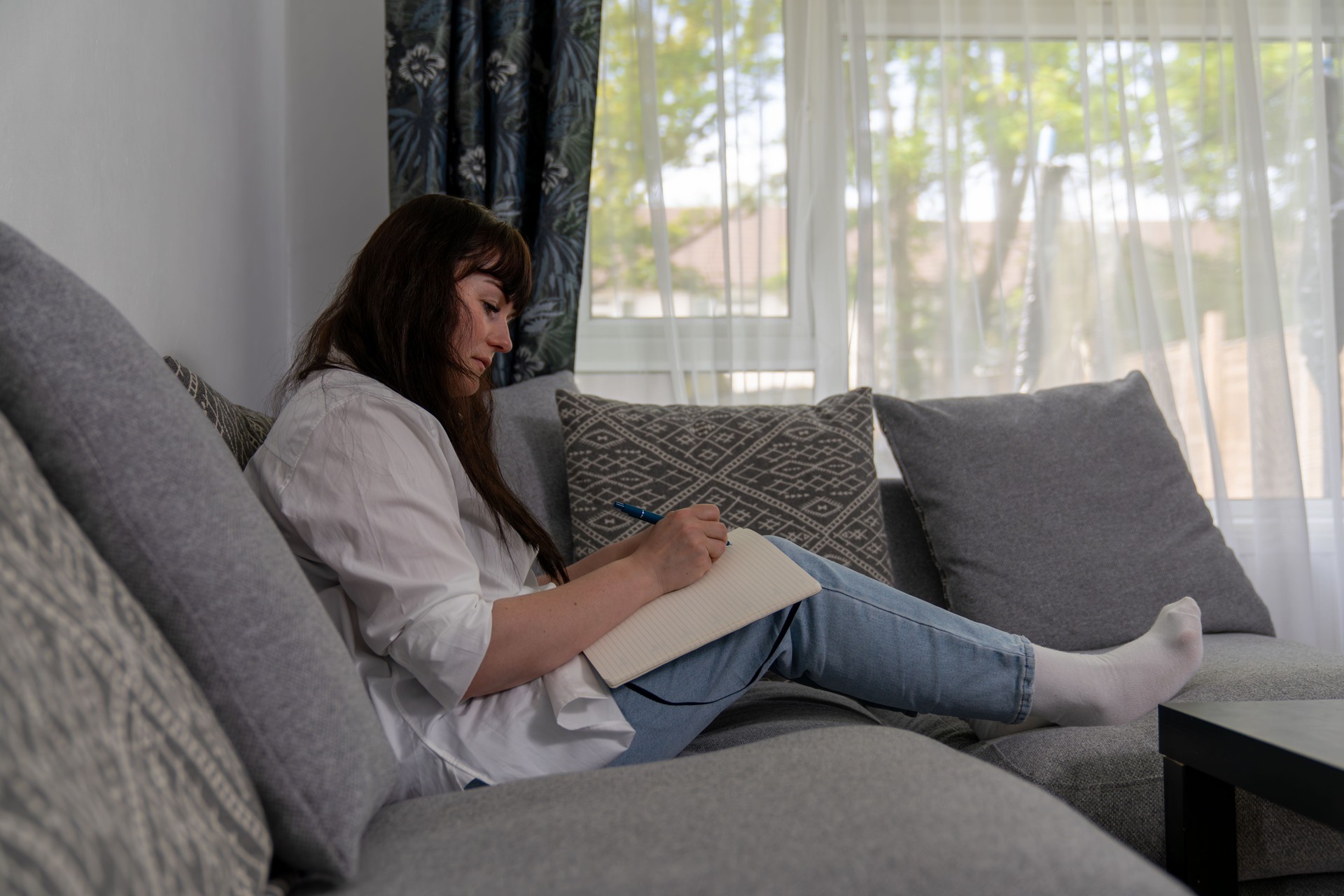 Woman writing on notebook sitting on sofa in living room