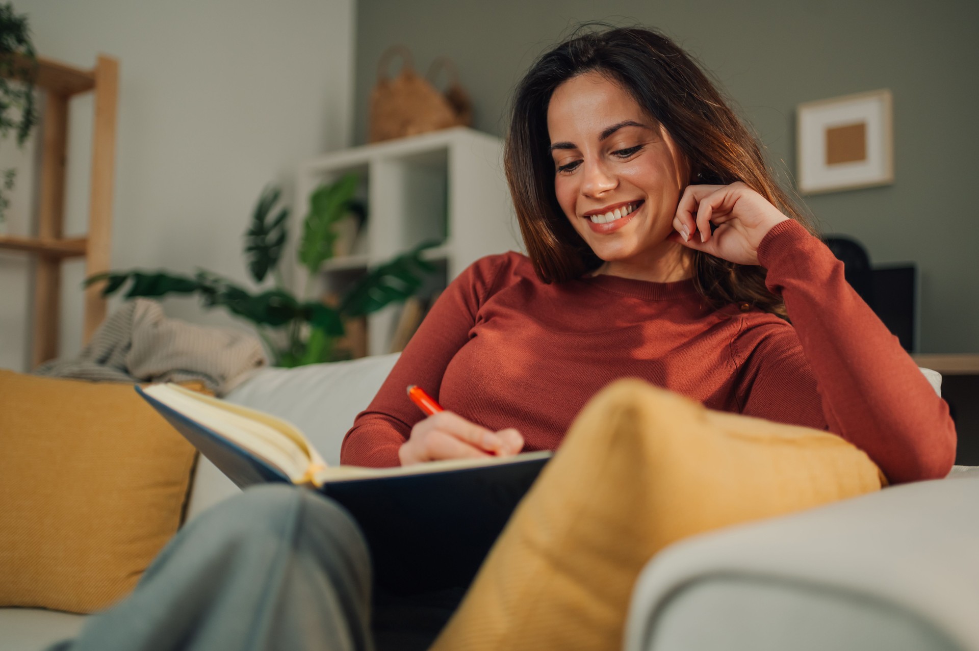 Young woman writing on notebook sitting on sofa at home