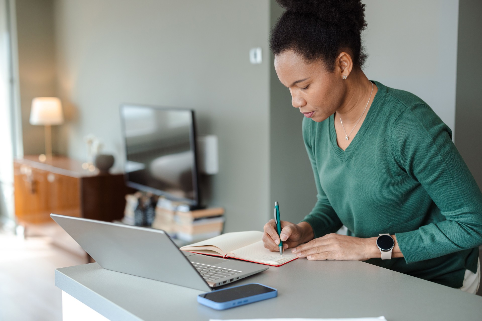 Focused woman writing notes while working on a laptop at home